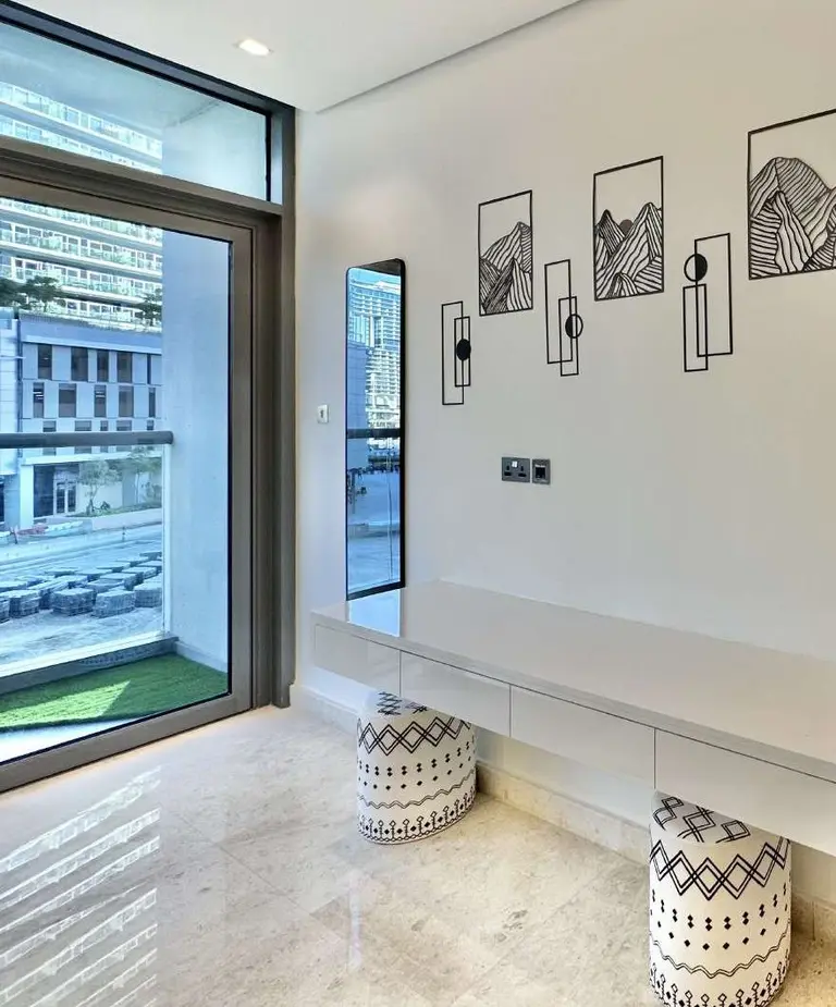 Bedroom corner with a floating desk, two patterned stools and line-art frames beside the window