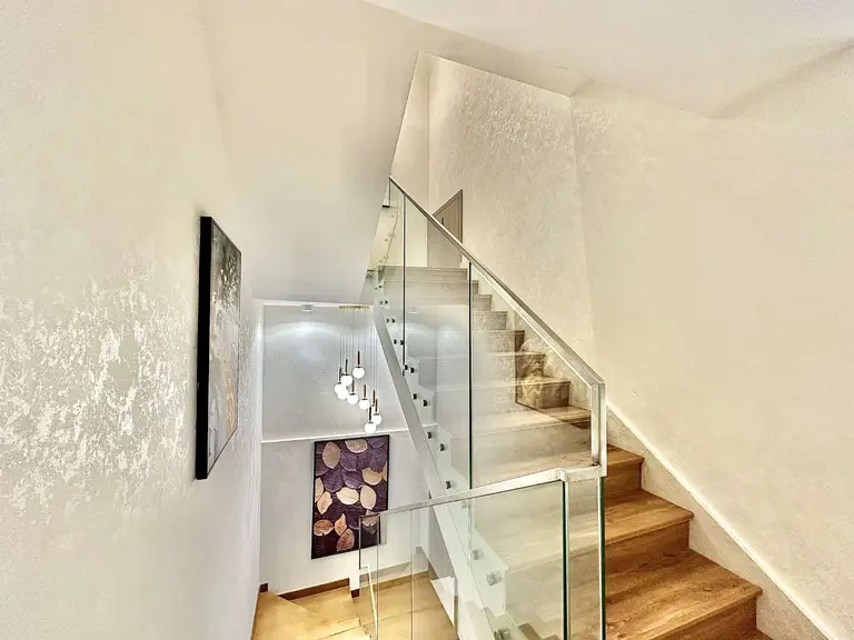 Staircase with wood-look treads, glass balustrade and a cascading pendant light