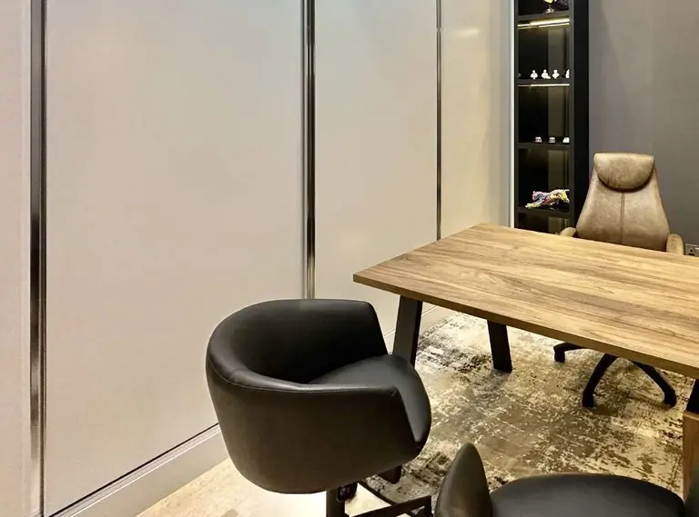 Office with a wooden desk, a leather desk chair and two armchairs on a patterned rug